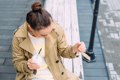 A young woman drinks a milkshake outdoors from a stylish glass jar with a straw