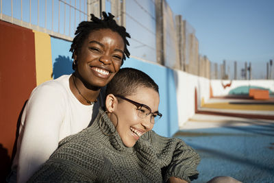 Female friends smiling while sitting at sports court