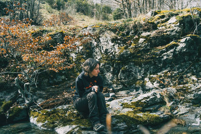 Portrait of a young girl sitting on a mossy rock next to a river in nature