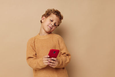 Boy using mobile phone against beige background