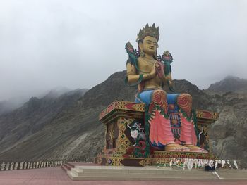 Statue against building and mountains against sky