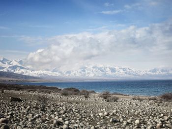 Lake by snowcapped mountains against cloudy sky