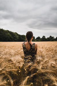 Rear view of woman sitting on field against sky