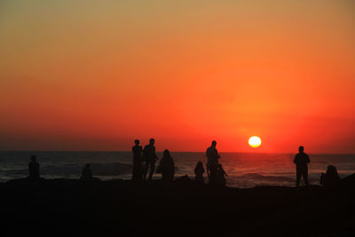 Silhouette people on beach against orange sky