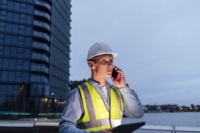Engineer with tablet pc talking on smart phone at dusk