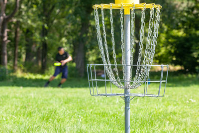 Disc golf player throwing a flying disc in the park, chain basket in the focus