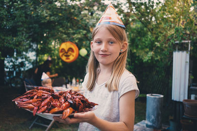 Portrait of girl holding plate with cooked crayfish at garden dinner party