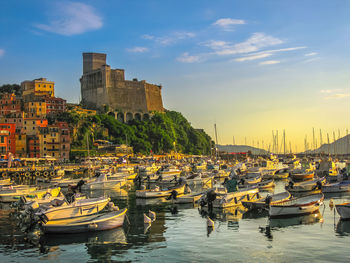 Boats moored at harbor by buildings against sky during sunset