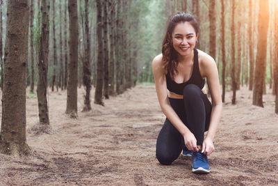 Portrait of smiling young woman tying shoelace in forest