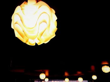 Low angle view of illuminated lanterns hanging against black background