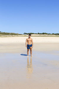 Full length of shirtless man walking on beach