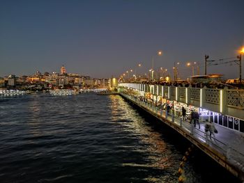 Illuminated buildings by river against clear sky