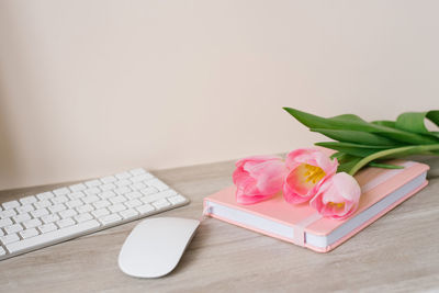 Workspace with keyboard, pink diary and pink tulips on wooden background. space for text