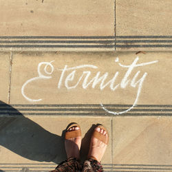 Low section of woman standing next to text on footpath