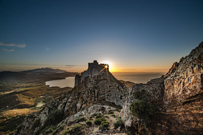 Scenic view of rocky mountains and sea against clear blue sky during sunset