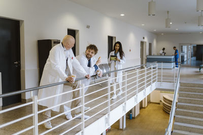 Smiling male doctors talking during coffee break by female colleague in hospital corridor