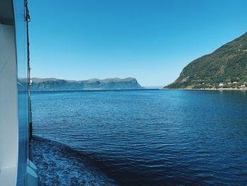 On a ferry, exploring norway  fjords, on a sunny day, mountains along the blue sea, clear blue sky 