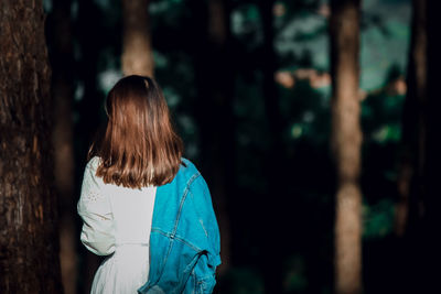 Rear view of woman standing by tree trunk in forest