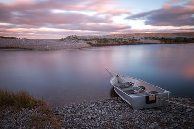Boat moored on shore against sky during sunset