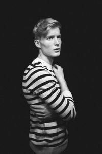 Portrait of young man standing against black background