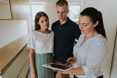 Woman explaining blueprint to couple on tablet at home