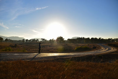 Man standing on road by field against sky