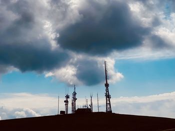 Low angle view of communications tower by building against sky