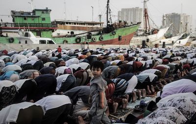 Side view portrait of boy standing amidst praying men at mosque