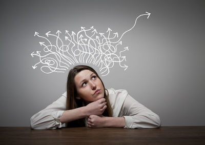 Portrait of young woman sitting on table against wall