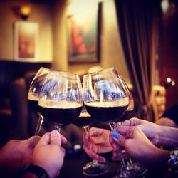 Close-up of hands toasting red wineglasses at home