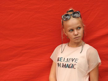 Girl looking away while standing against orange textile