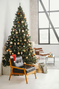 Cozy armchair near christmas tree in sunny room with big windows. santa's hat nobody christmas tree