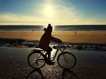 Side view of silhouette woman riding bicycle at beach during sunset