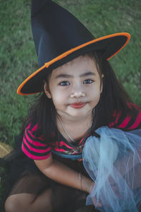 High angle portrait of girl wearing witch hat sitting on field