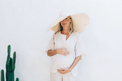 A beautiful pregnant woman in white clothes touches her belly.