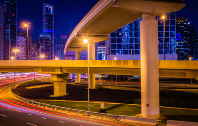 Light trails by illuminated bridge in city at night