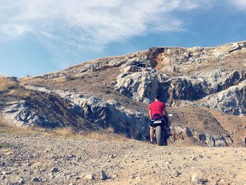 Rear view of men with motorcycle on mountain against sky