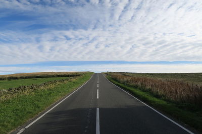 Empty road amidst field against sky