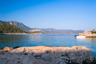 Scenic view of river by mountains against clear blue sky