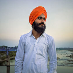 Young man looking away while standing against sky