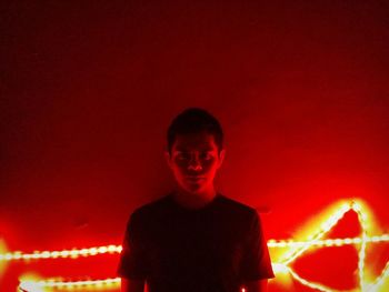 Portrait of man standing against illuminated red wall