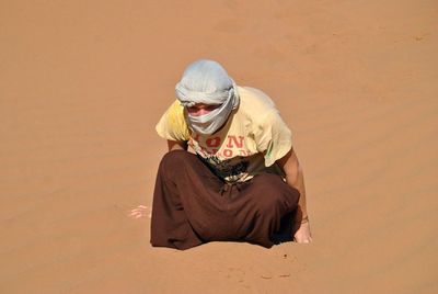 High angle view of man wearing headscarf sitting on sand at desert