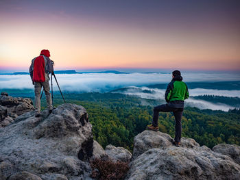 Man standing on rock against sky during sunset