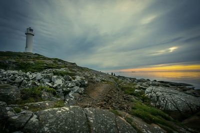 Lighthouse on beach against cloudy sky