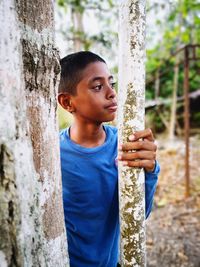 Thoughtful boy standing by tree trunk