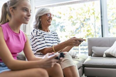 Happy grandmother playing video game with granddaughter at home