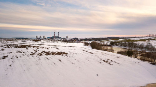 Snow covered land against sky during sunset