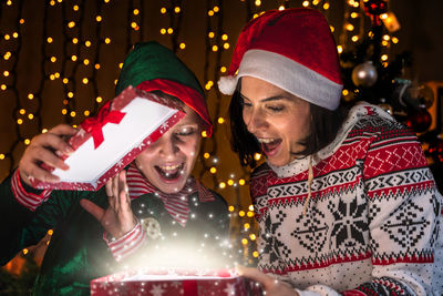 Portrait of smiling friends standing against illuminated christmas