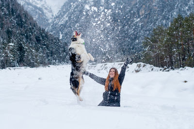 Cheerful woman playing with dog on snow covered field