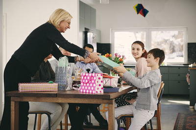 Grandmother giving gift to boy sitting with family at dining table